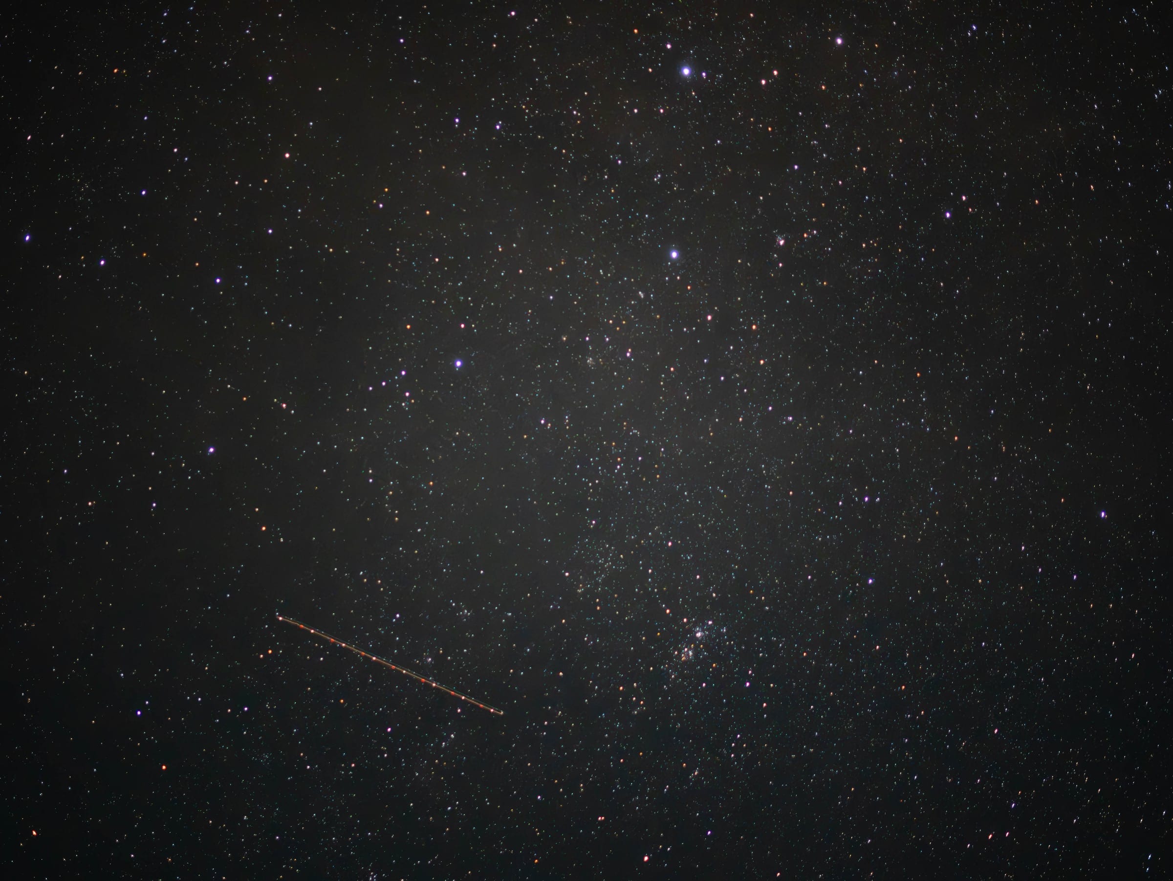 A faint meteor streaking across a dense, dark field of stars.