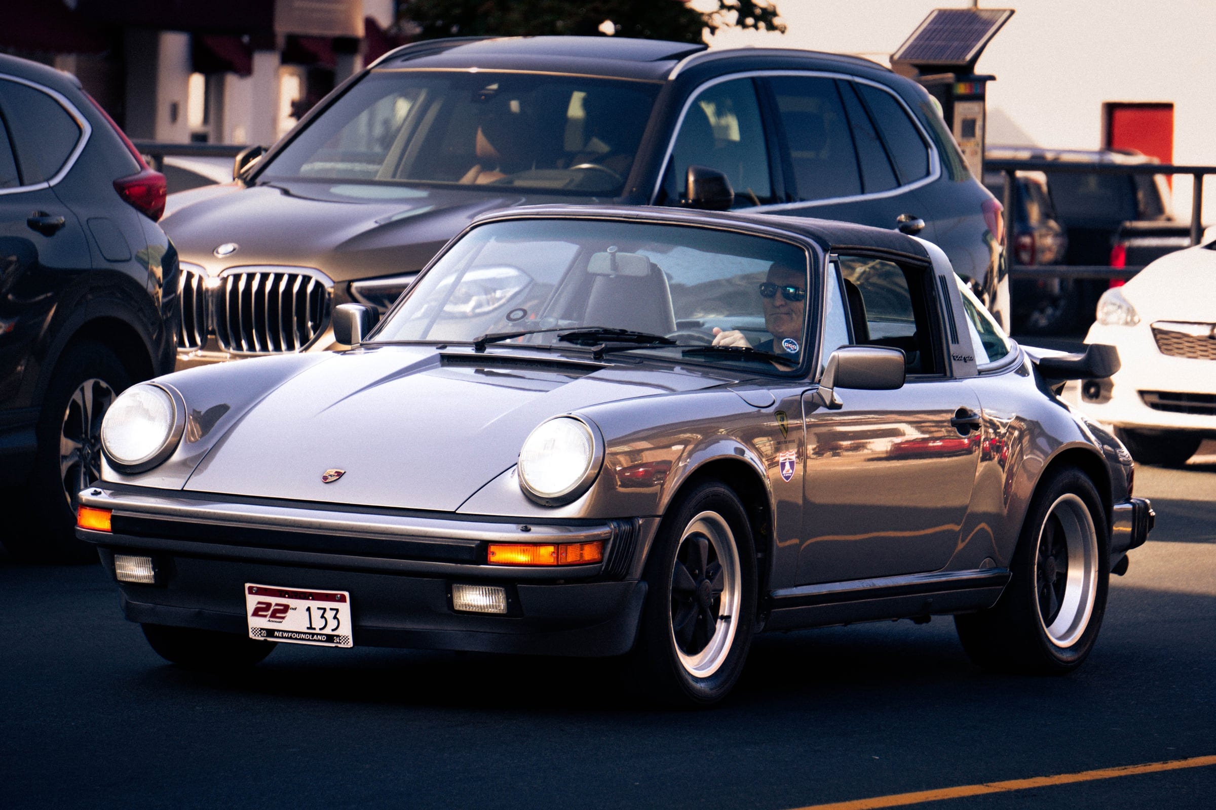 A silver classic Porsche 911 in traffic, a BMW close behind.