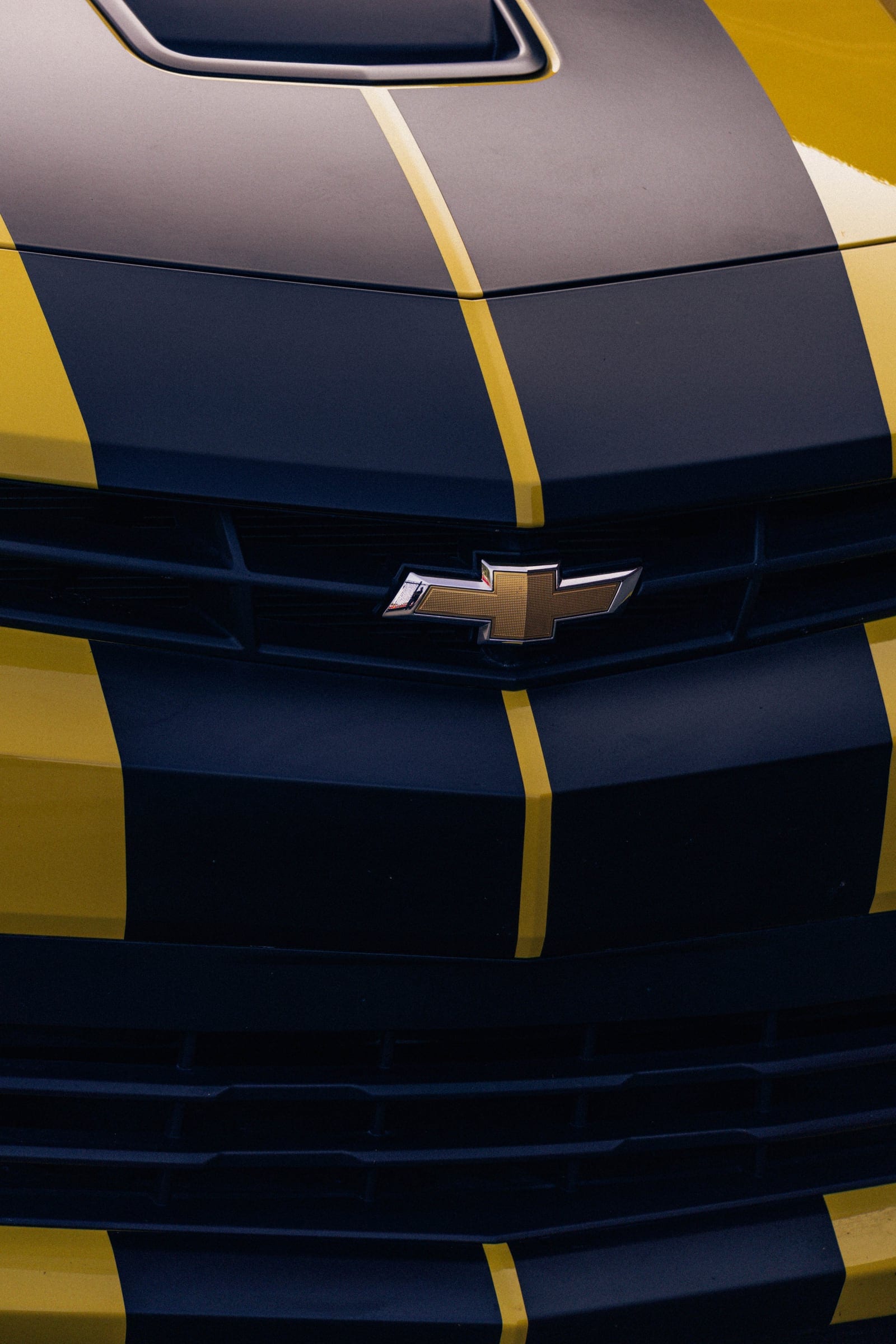 Close view of a yellow Camaro’s bonnet and grille, split by black stripes around the Chevrolet badge.