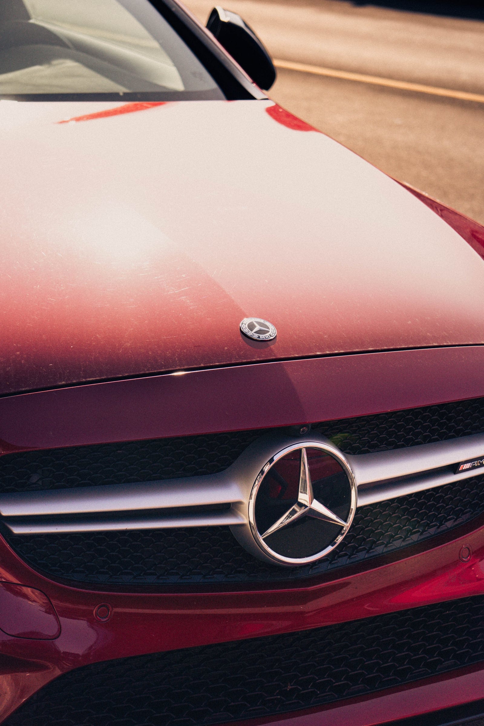 The glossy red bonnet and chrome grille of a Mercedes-Benz, light washing across the paint.