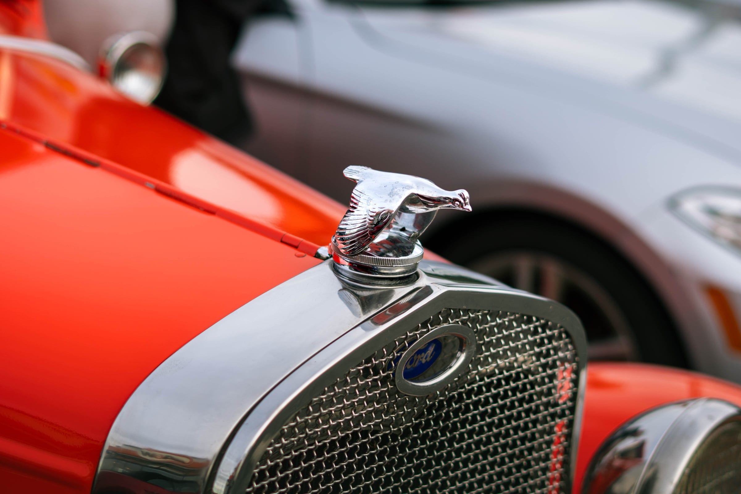 A chrome hood ornament on a vintage car, the grille soft behind it.