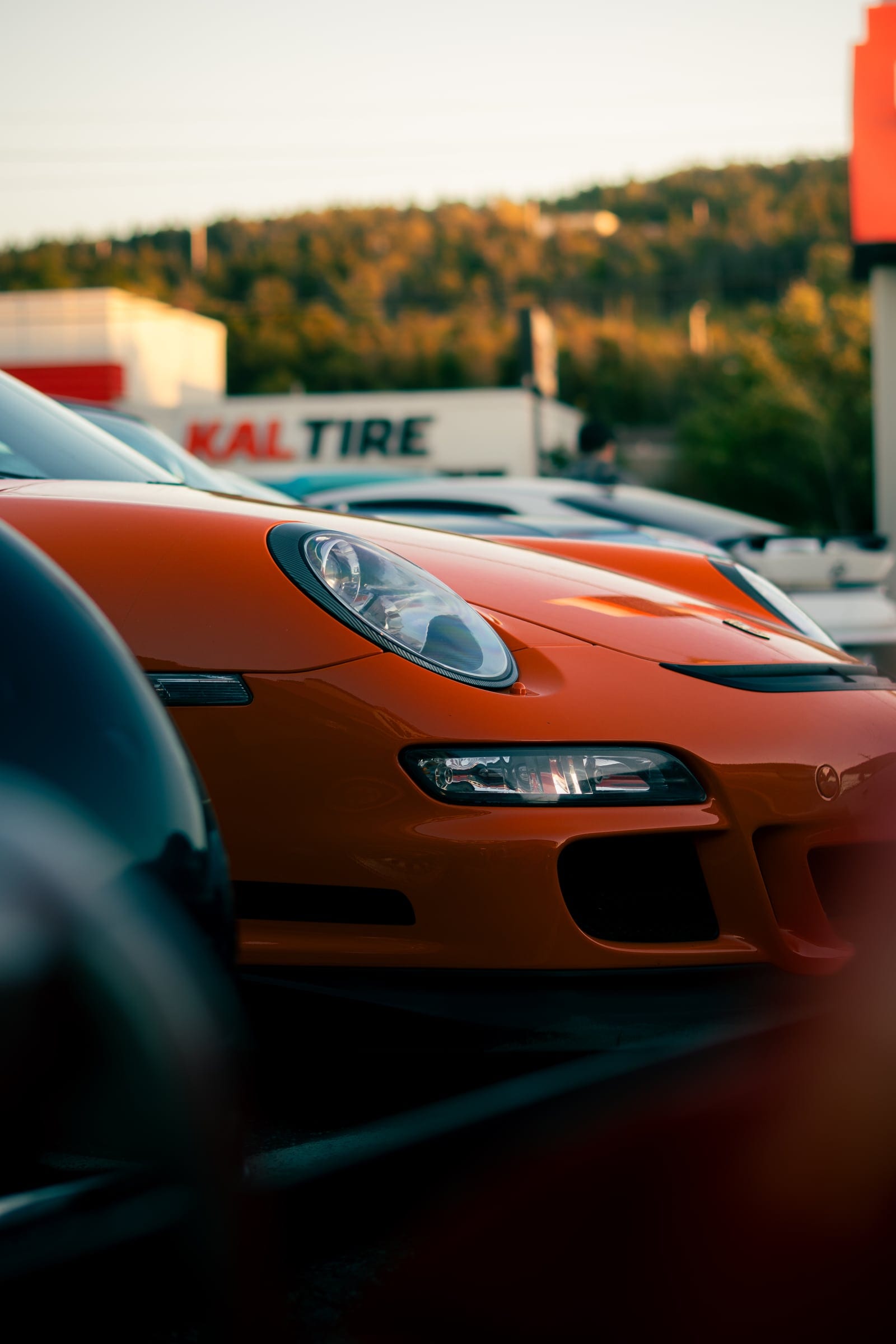 The front of an orange Porsche GT3 seen past a blurred car in the foreground.