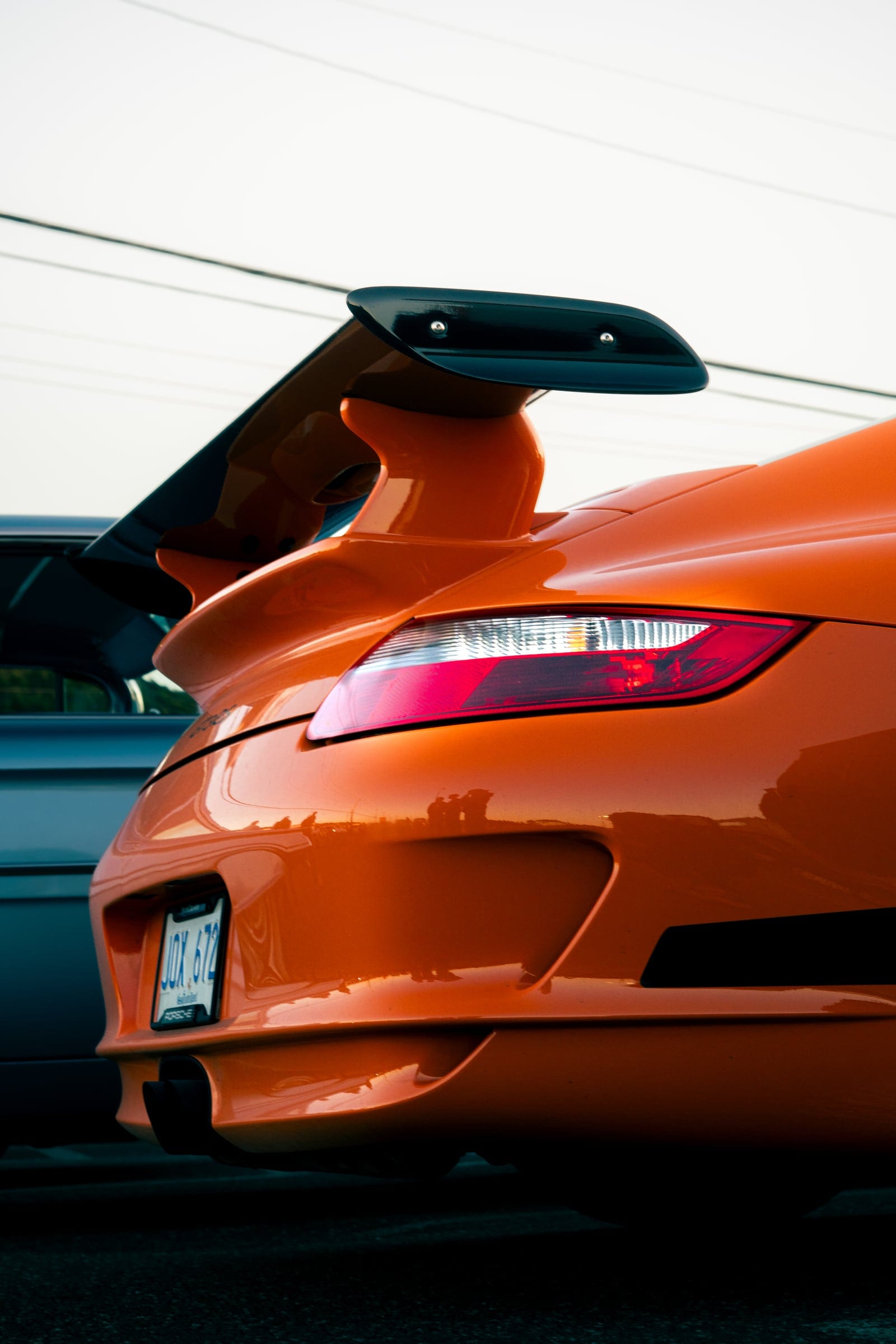 The rear wing and tail light of an orange Porsche GT3 against a pale sky.