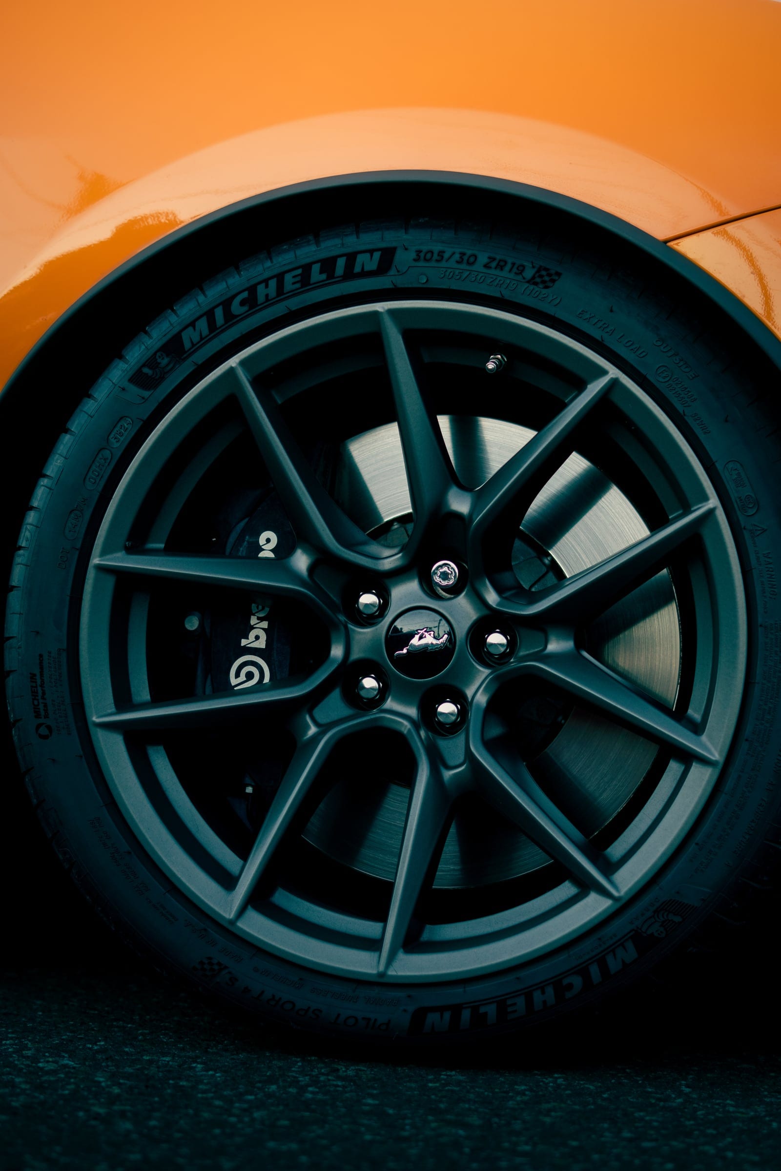 A dark alloy wheel and brake caliper under an orange wheel arch.