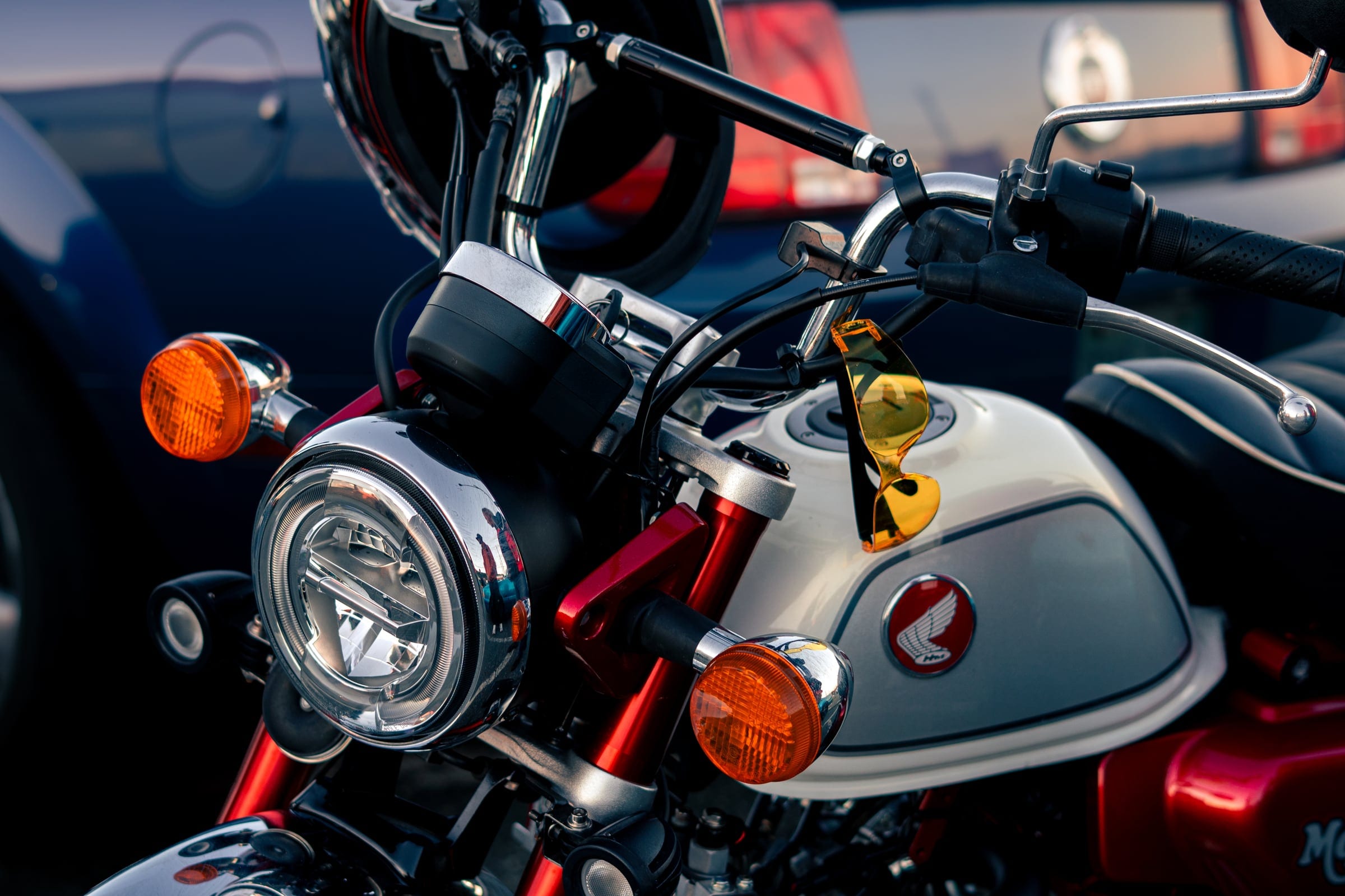 The headlight, indicators and handlebars of a small red and white Honda.