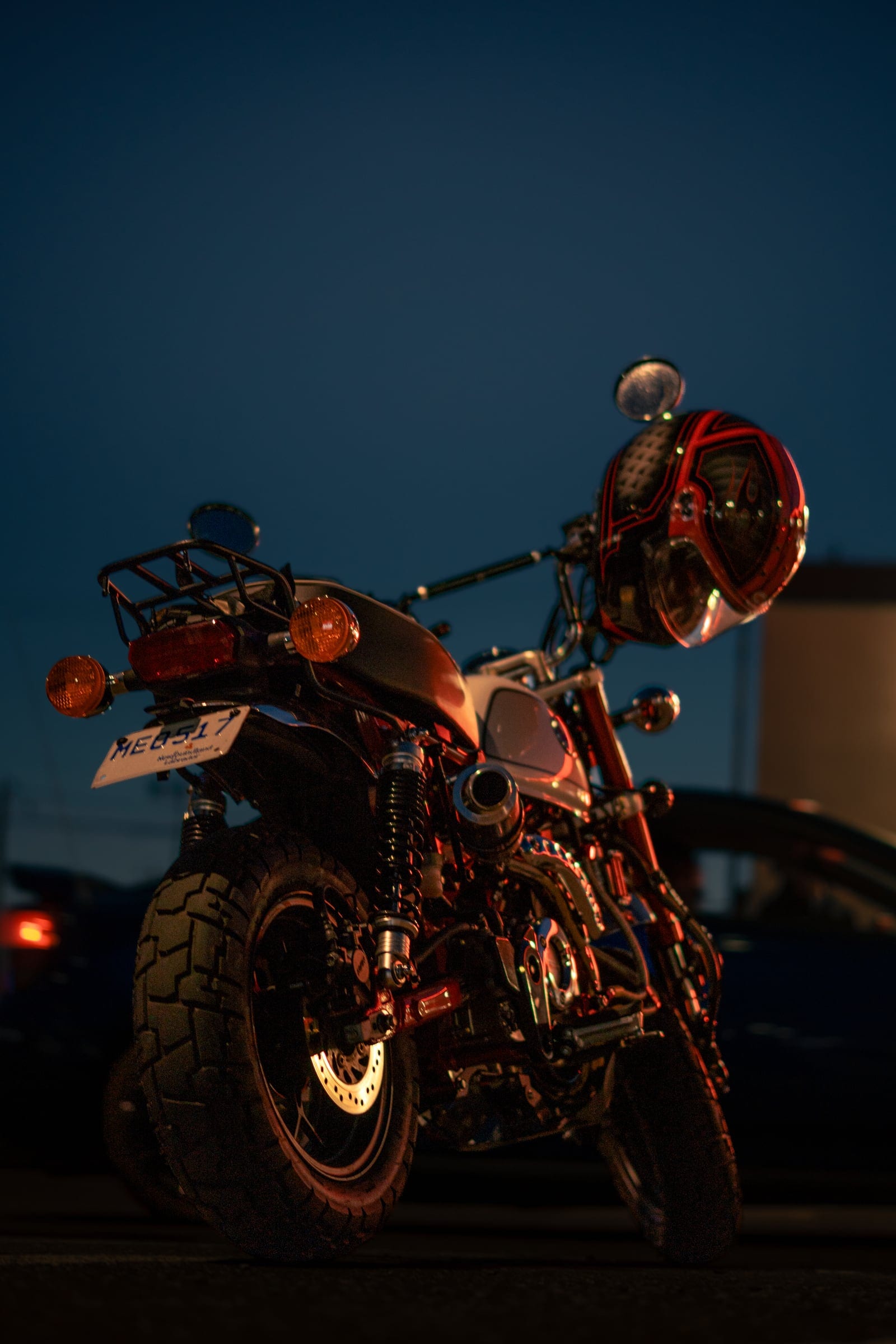 A motorcycle silhouetted against an orange sky, people standing beyond it.
